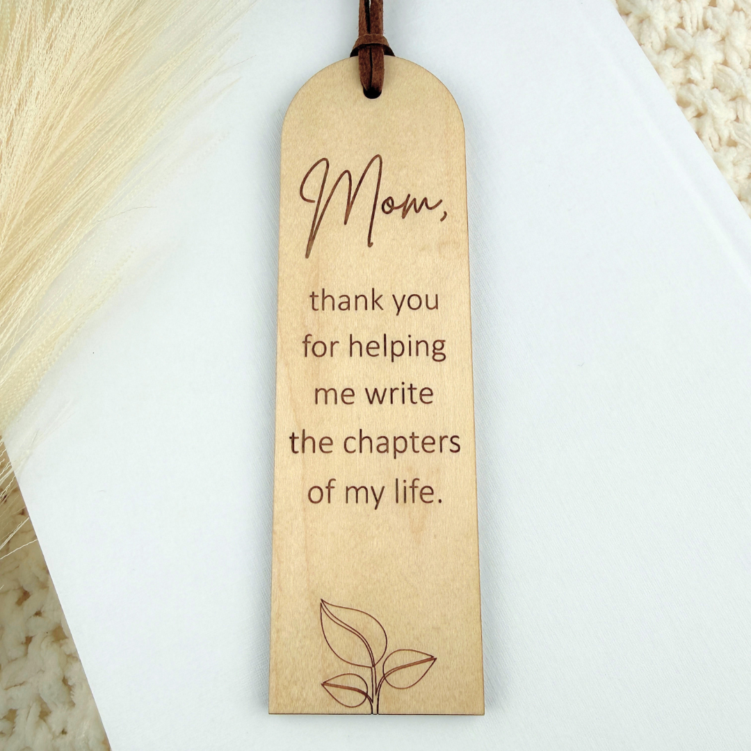 Maple wood bookmark with a mom engraved quote on a white book.