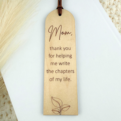 Maple wood bookmark with a mom engraved quote on a white book.