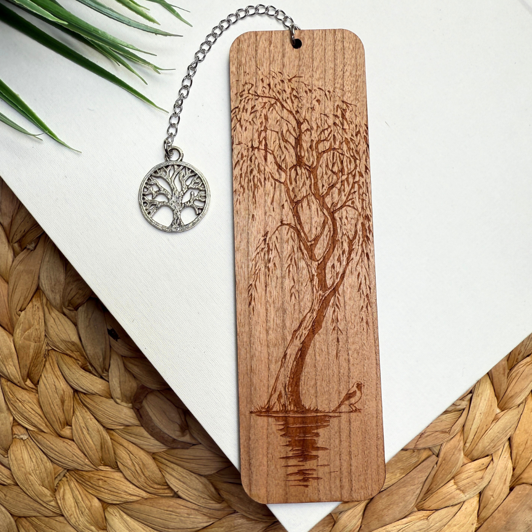 Cherry wood bookmark with engraved tree design and chain, placed on a woven surface.
