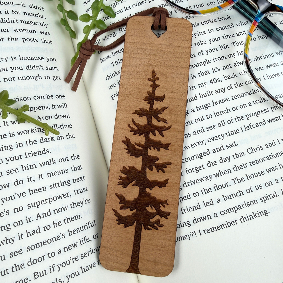 Wooden bookmark with tree design on a book page, cherry wood and brown faux suede rope.