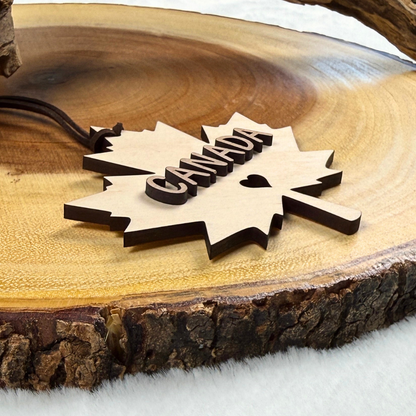 Layered maple and walnut Canadian maple leaf wood ornament resting on a wood slice.