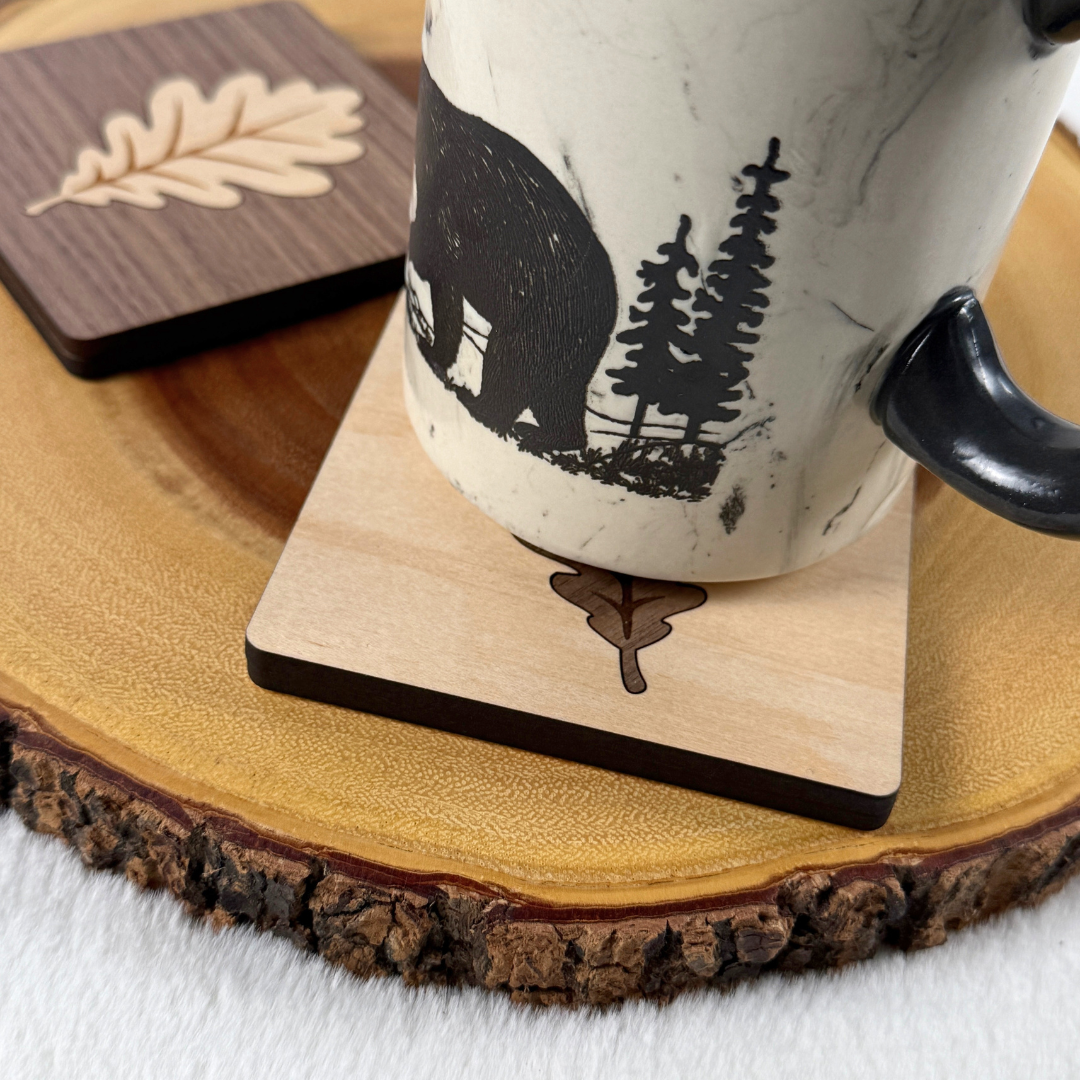 Coffee mug resting on a handmade wood coaster with an oak leaf inlay, displayed on a natural wood slice.