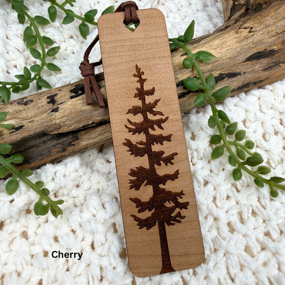 Engraved cherry wood bookmark with tree design on a white surface with greenery.