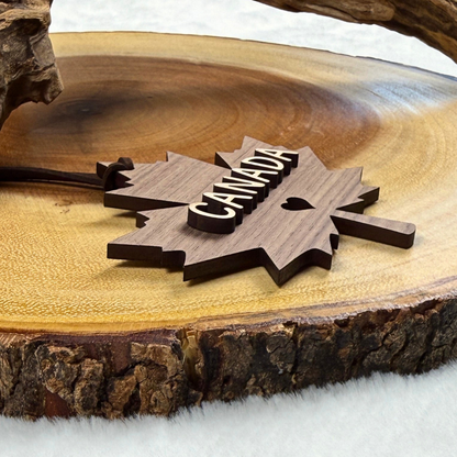 A walnut wooden maple leaf ornament with the word 'CANADA' and a small heart, displayed on a rustic wood slice with white faux fur underneath.