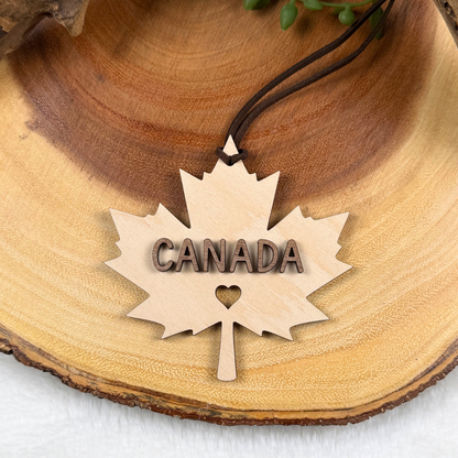 Maple leaf ornament with raised walnut CANADA lettering and heart cutout with brown faux suede rope.
