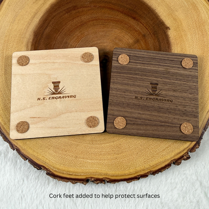 Backs of maple and walnut wood coasters showing protective cork feet and engraved maker details.