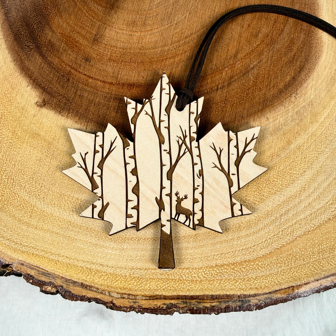 Maple wood Canadian maple leaf ornament with engraved deer and birch forest. Handmade and finished with a brown faux suede rope.