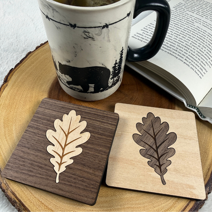 Maple and walnut oak leaf inlay coasters displayed side by side with a coffee mug.