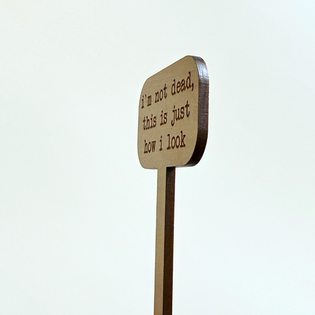 Wooden plant stake sign showing the thickness with humorous text on a white background