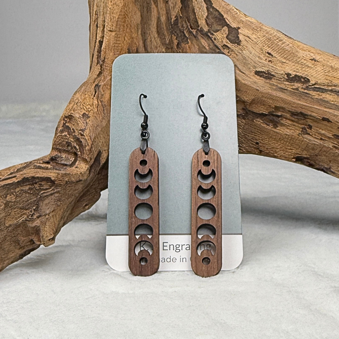 Walnut wood earrings with laser cut crescent moon. Dangle earrings with black stainless steel hooks and silicone backers. Finished with natural wood oil. placed on an earring card.