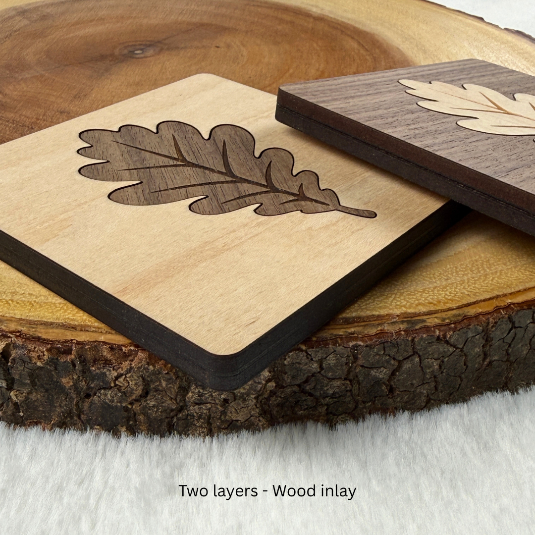Angled view of handmade maple and walnut wood coasters showing their contrasting oak leaf inlays. Two layers.