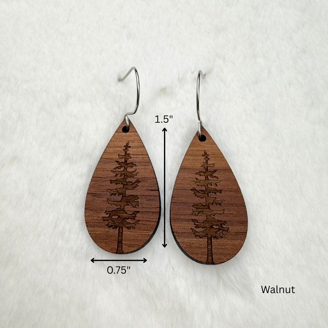 Teardrop-shaped wooden dangle earrings with a laser-engraved pine tree design, shown on a white textured background with dimension labels (0.75 inches wide, 1.5 long