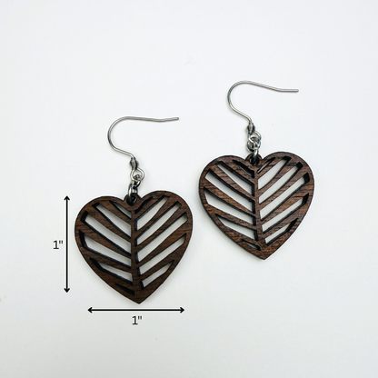A pair of heart-shaped wooden drop earrings with a cutout pattern and stainless steel hardware, shown on a white background with dimension arrows indicating 1 inch by 1 inch.