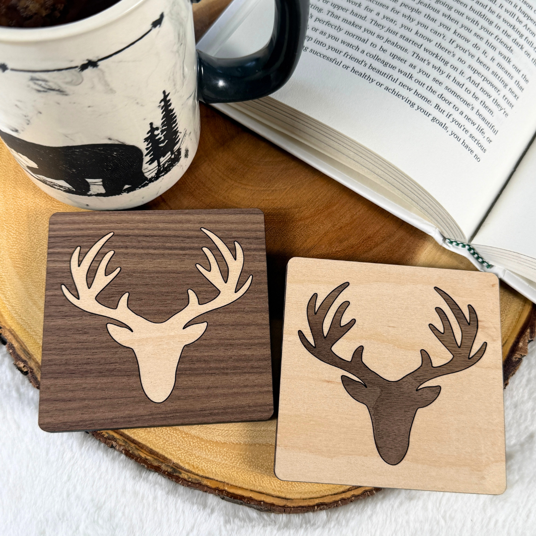 Both deer inlay coaster colour combinations displayed beside a mug and an open book.